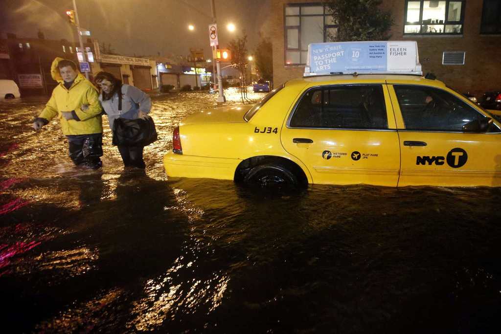 Pedestrians walk past a submerged taxi in Brooklyn, New York, as Hurricane Sandy made landfall in the northeastern United States. Hurricane Sandy began battering the U.S. East Coast on Monday with fierce winds and driving rain, as the monster storm shut down transportation, shuttered businesses and sent thousands scrambling for higher ground hours before the worst was due to strike.