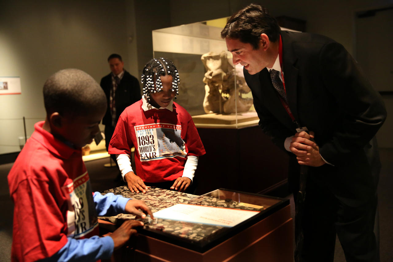 Jim Holstein, collection manager of meteorites and mineralogy at the Field Museum talks with Simone Leflore, 9, from Leif Ericson Elementary Scholastic Academy and tells her about the Madrepore marble that they are standing over and touching.