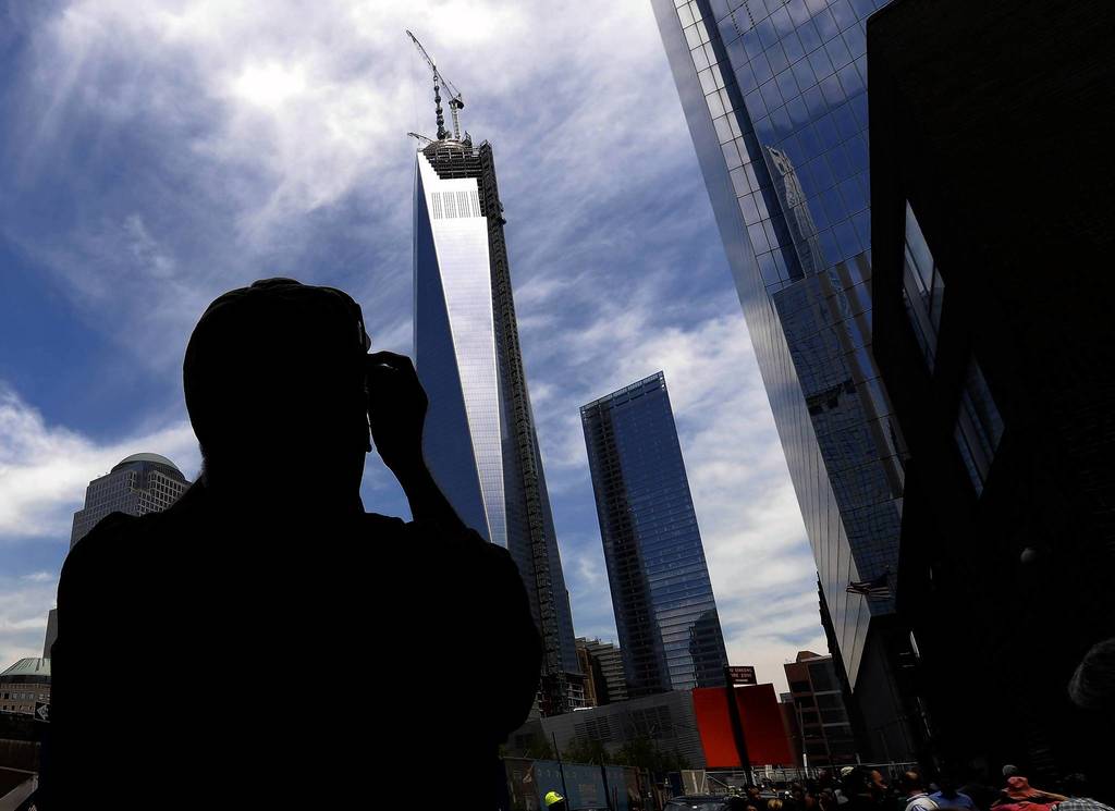 A passerby takes a photo of One World Trade Center as the final section of the spire is placed atop the building.