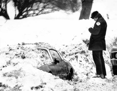 Discovering a buried car that seems to have been parked on Stockton Drive in Lincoln Park for a long time, a policeman writes out a parking ticket on Jan. 23, 1979. The officer had to clear the snow away from the license plate to read the number.