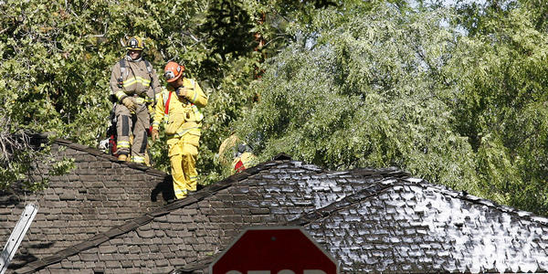 Firefighters walk on the roof of a home affected by a fire sparked in ...