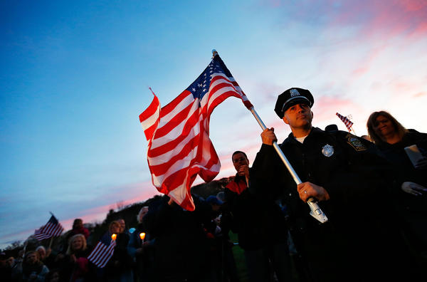 Watertown Police officer Brandon O'Neill holds a large American flag during a candlelight vigil at Victory Park in Watertown, Mass., Saturday. A manhunt for Dzhokhar A. Tsarnaev, 19, a suspect in the Boston Marathon bombing, ended after he was apprehended Friday night on a boat parked on a residential property in Watertown. His brother Tamerlan Tsarnaev, 26, the other suspect, was shot and killed after a car chase and shootout with police in Watertown early Friday morning.
