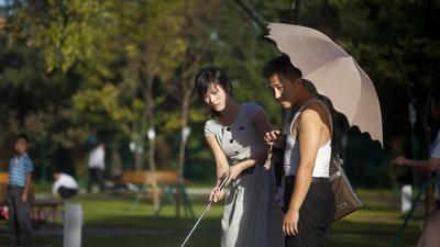 In this Sept. 8, 2012, photo, a man holds a woman's bag and parasol as they play miniature golf at a newly built amusement park in Pyongyang, North Korea.