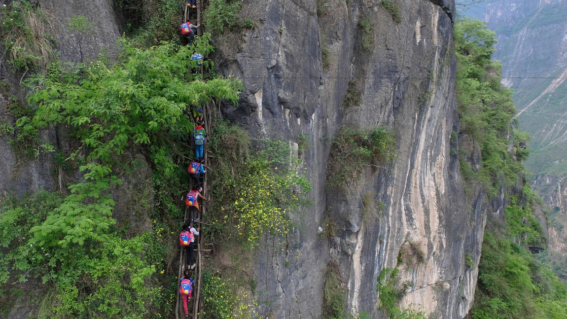 Children carry their school backpacks as they climb a cliff on their way home from school in Zhaojue county