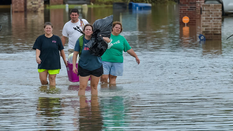 People wade in water near flood-damaged homes in Youngsville, La.