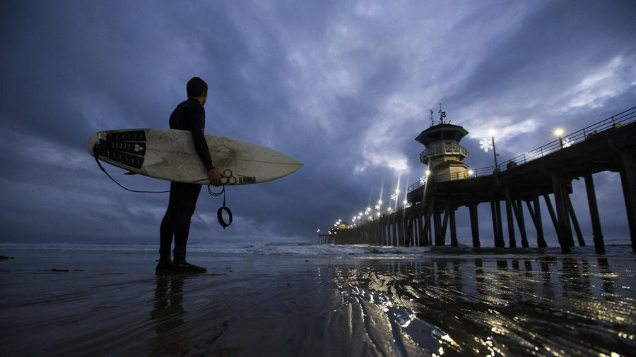 Nhân viên cứu hộ kiêm vận động viên lướt sóng – Jachin Hamborg ngắm nhìn bầu trời kỳ ảo và những đợt sóng sau khi anh lướt sóng trong ca làm dưới hoàng hôn bên đê biển Huntington. (Allen J. Schaben / Los Angeles Times)