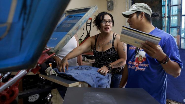 Diego Maria, right, talks with Ana Laura Lopez as she screen-prints T-shirts at a shop Maria opened