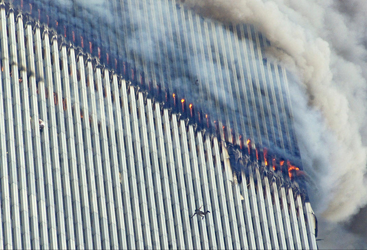 A person jumps from the burning North Tower of the World Trade Center as another clings to the outside, left center.