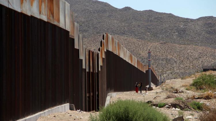 In May, a Mexican family stands next to the border wall between Mexico and the United States, in Ciu