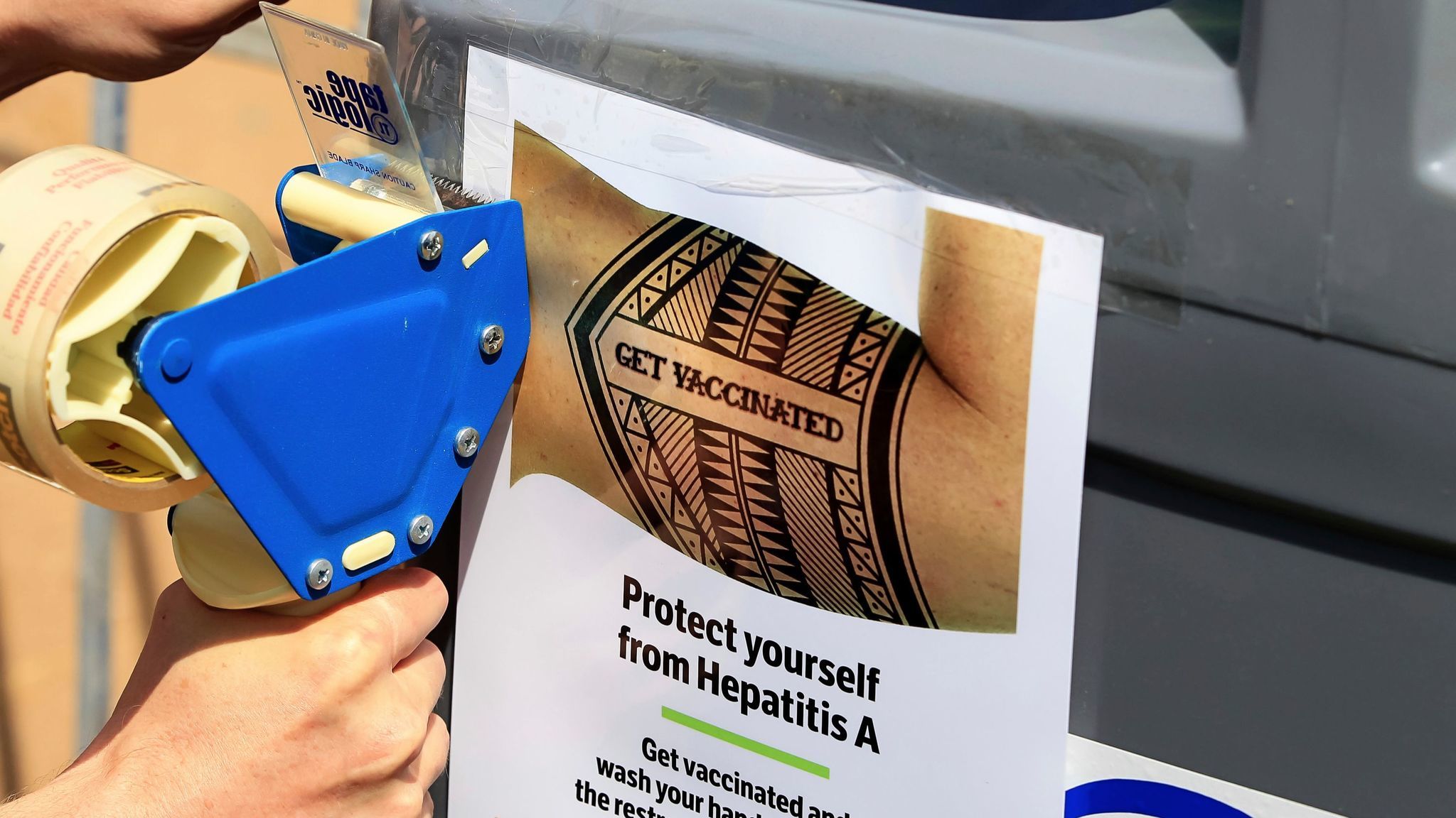 A worker tapes signage telling people to get vaccinated to protect themselves against Hepatitis A in downtown San Diego.