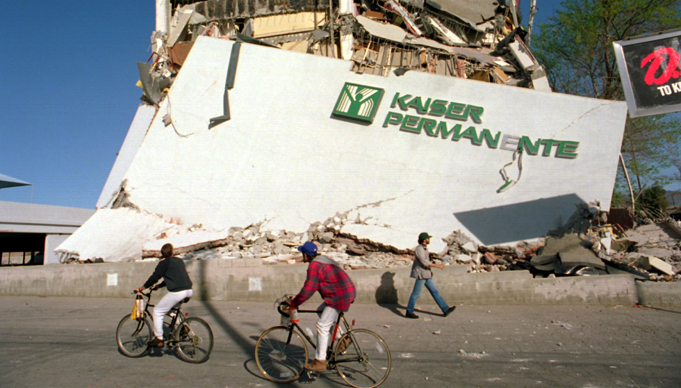 Cyclists roll past the remains of a collapsed Kaiser Permanente clinic and office building in Granada Hills following the Northridge earthquake.