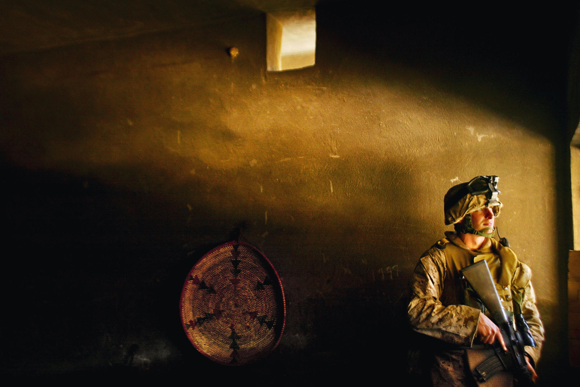 A U.S. Marine stands watch as others take a moment to rest after taking over two houses in a pre–dawn mission in the Jolan Heights area of Fallouja, Iraq in 2004.