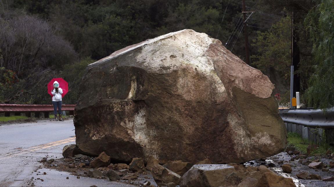 Gina Picciolo takes a picture of a boulder that fell onto Topanga Canyon Boulevard near Grandview Drive in the Fernwood area on Jan. 23, 2017. Picciolo is a longtime resident in the area.