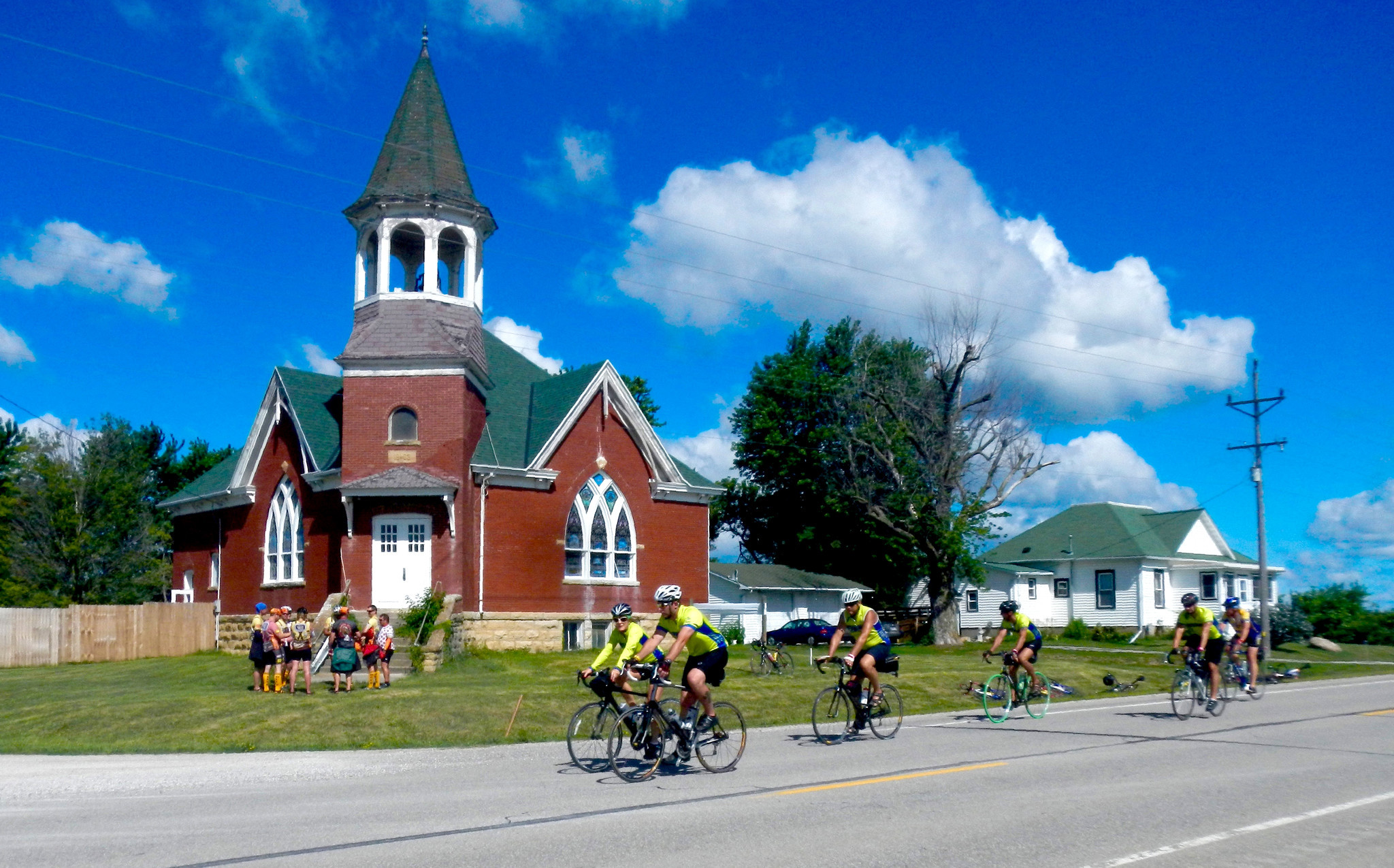 Cyclists on an Iowa RAGBRAI tour riding by a church in a small town in eastern Iowa. Some of the riders have stopped to check out the church.