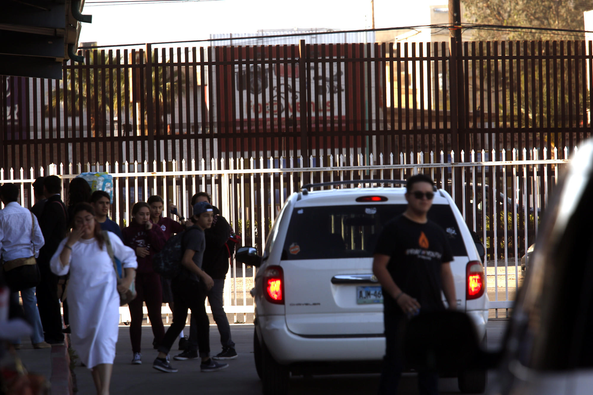 Students are dropped off and picked up in an area framed by the school fence in white and the brown U.S.-Mexico border fence.