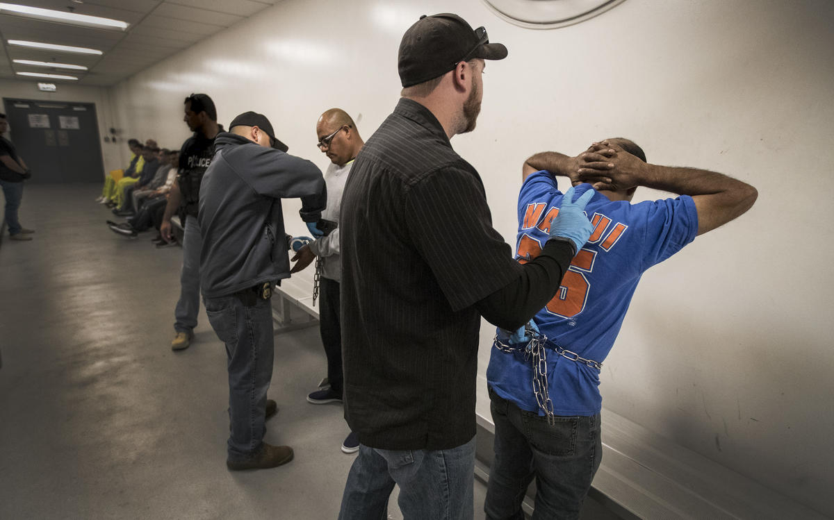 ICE agents search Esteban Amigon, center left, and Sergio Rodriguez, right, as the men are processed at the ICE downtown staging facility in Los Angeles.