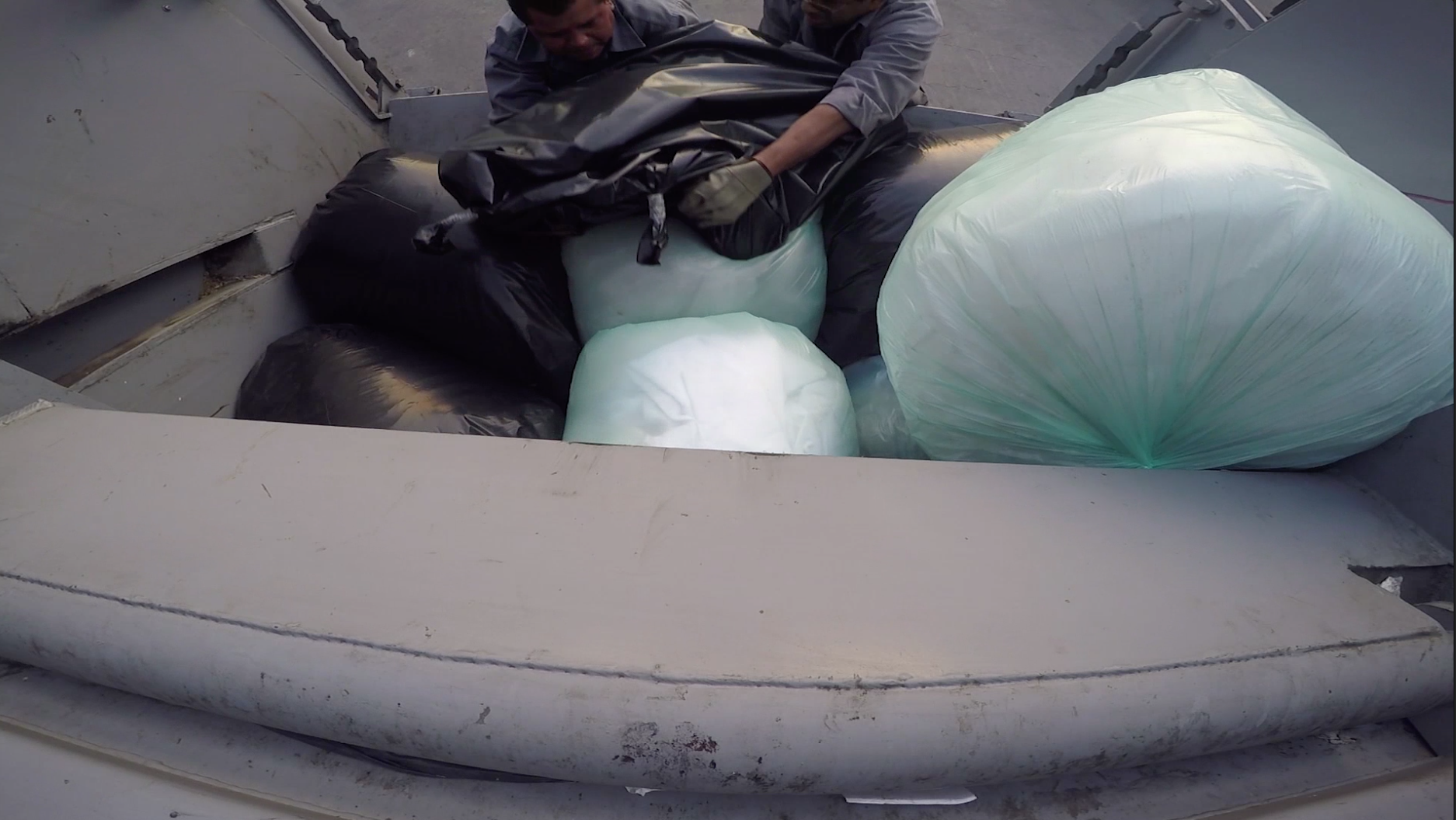 A video still of sanitation workers loading artist Regina Jose Galindo, in a garbage bag, as part of a performance called "Desecho."
