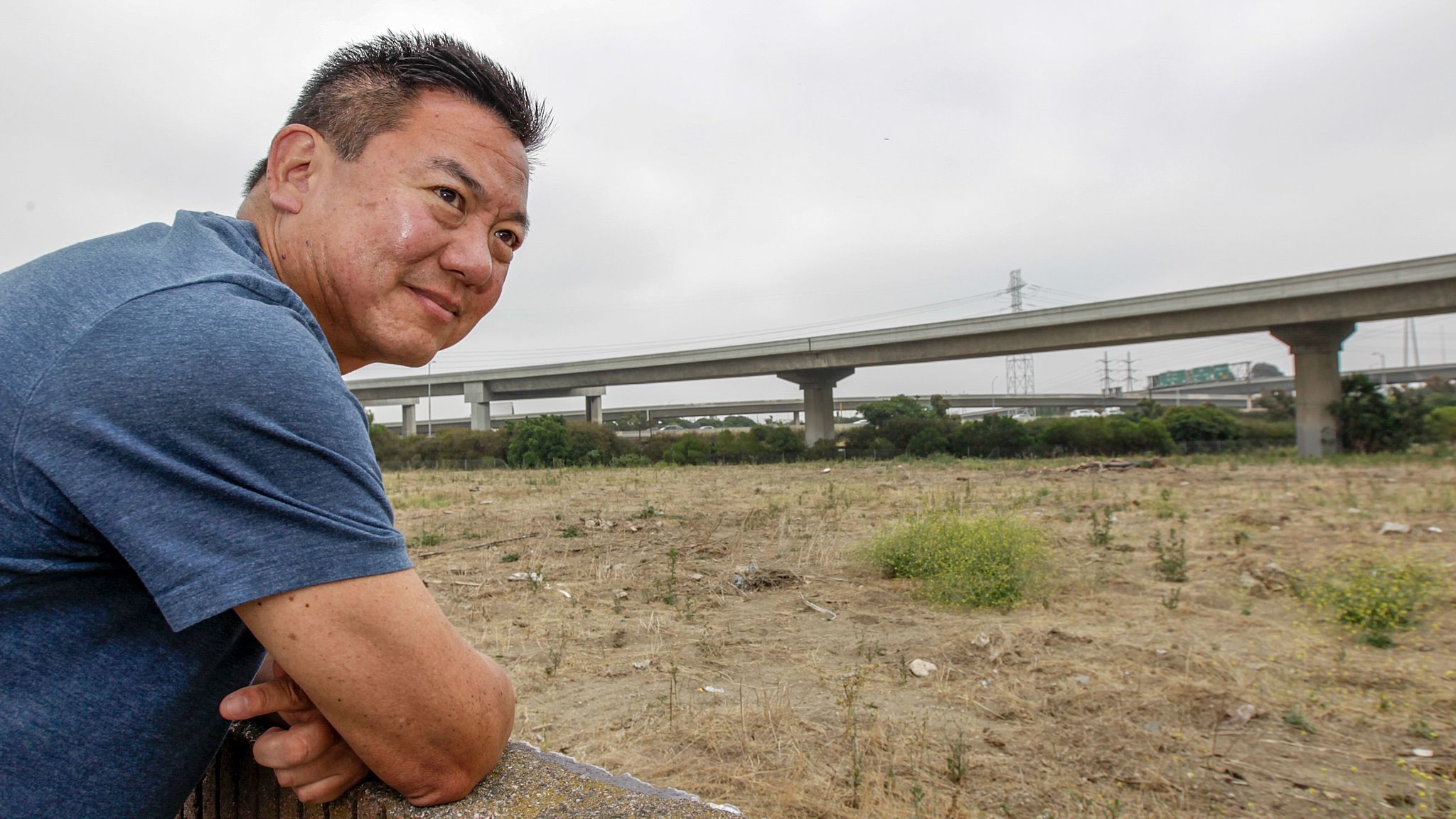 Harbor Gateway resident Craig Kusunoki looks from his backyard wall onto the site of a proposed 15-home subdivision planned near the interchange of the 110 and 91 Freeways. Opponents say future residents will face noise and air pollution from nearby cars and trucks.