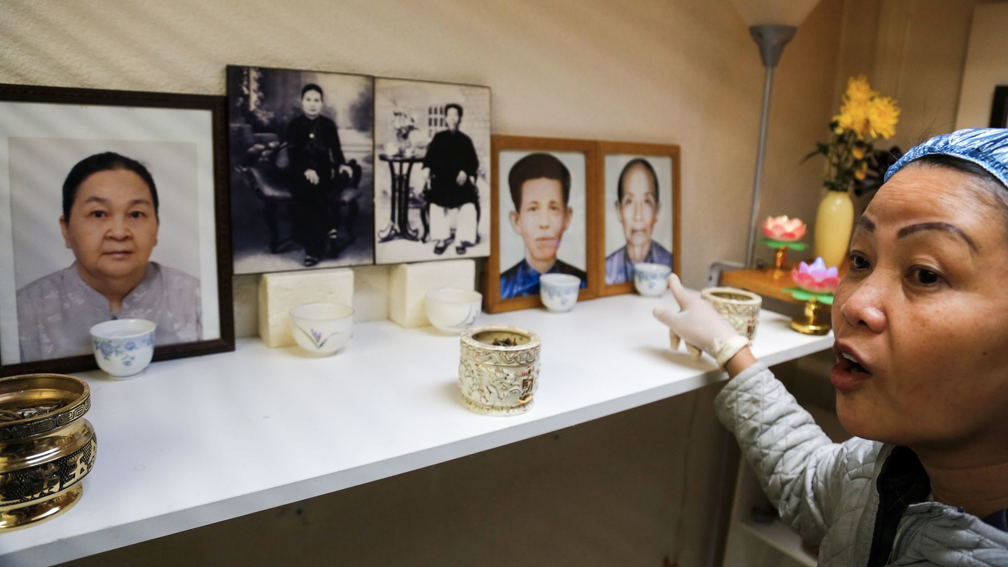 Hue Phan points to pictures of her and her husband's parents and grandparents arranged for a home shrine.