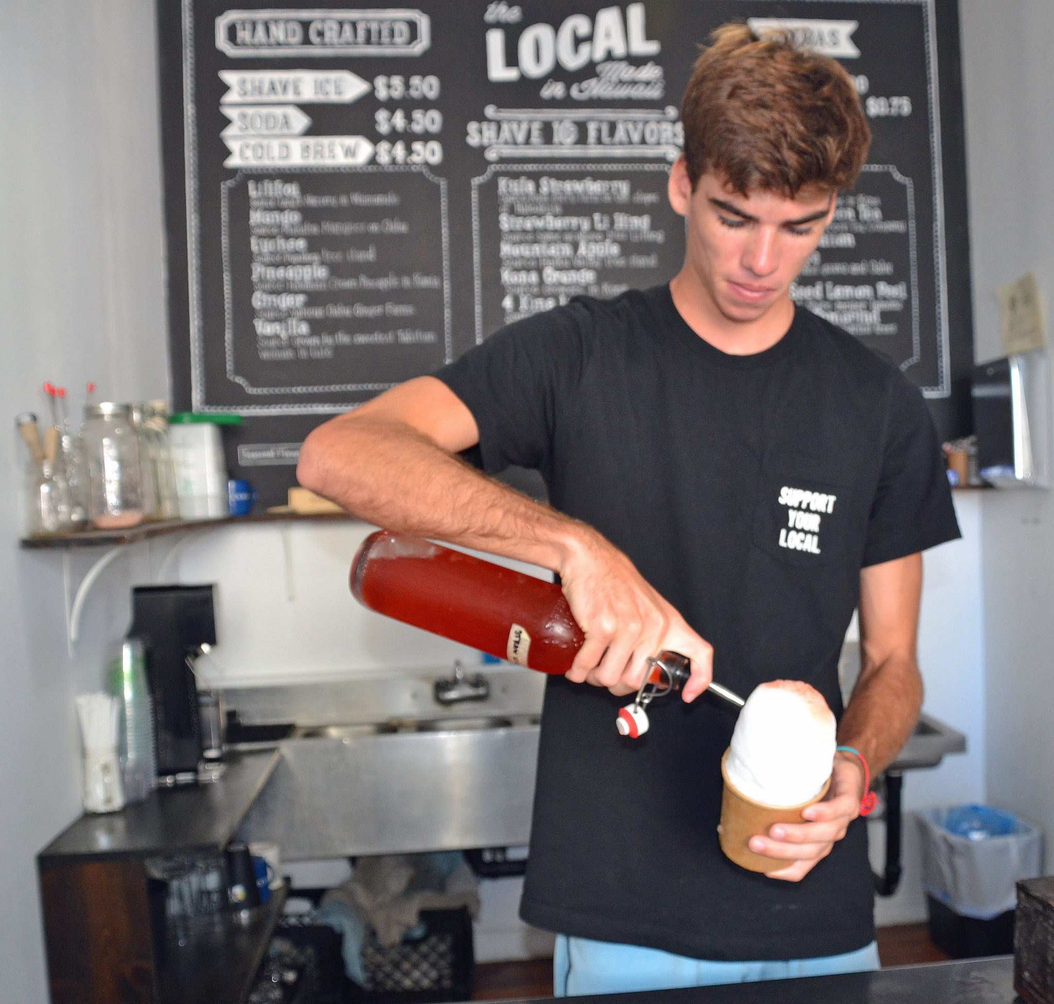 Caleb Carter pours strawberry flavored with li hing over shave ice in a cup.