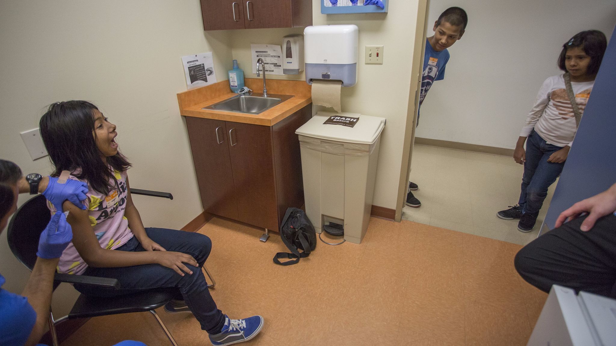 Gilbert Jr., 12, and Faith, 9, watch as their sister Carla Acosta, 11, is vaccinated by medical technician Ricardo Vasquez at Children's Hospital Los Angeles.
