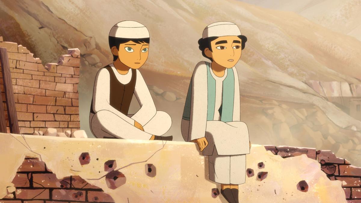Image is from the film 'The Breadwinner' (2017). A still from a 2D animated film with a simplistic cartoon style. Two young girls with short hair cuts, dressed in clothes traditionally worn by men in Afghanistan, sit on a crumbling brick wall looking out past the frame. A mountain can be seen in the background.