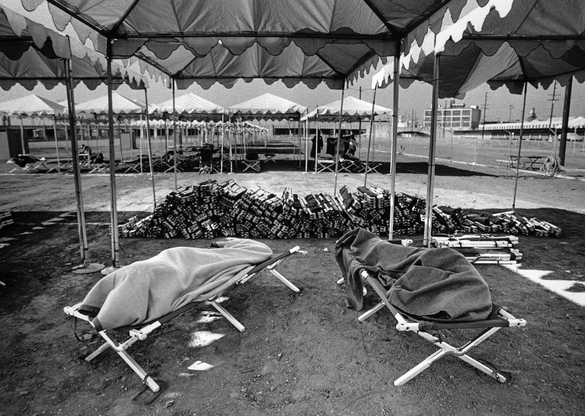 June 16, 1987: Two people sleep while a stack of cots go unused at the