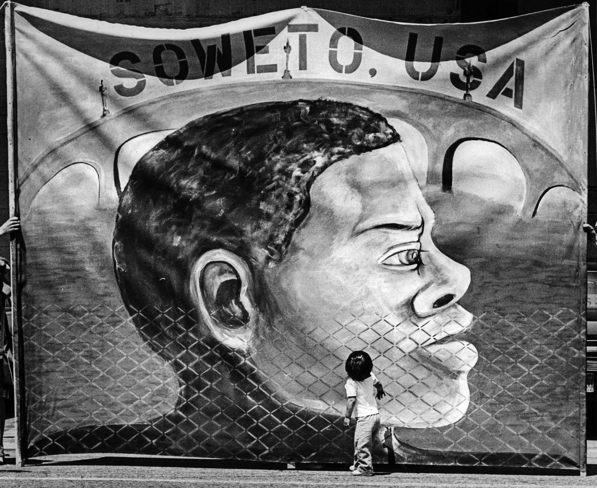 June 15, 1987: Child gazes at banner displayed by protestors outside of the Urban Campground. Protes