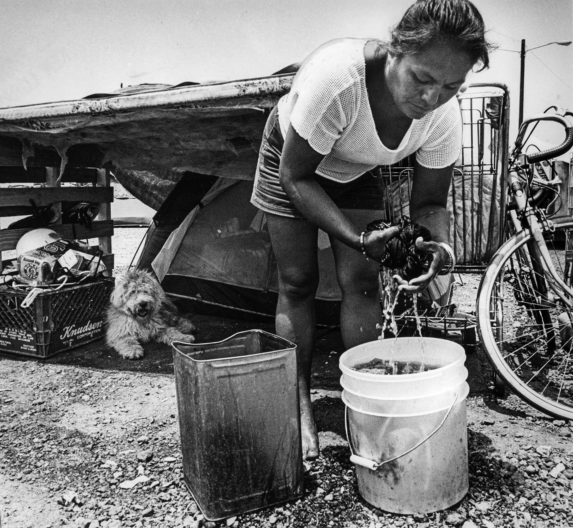 June 26, 1987: Esperanza Huerta washes clothes in front of tent while her dog Snowball takes it easy