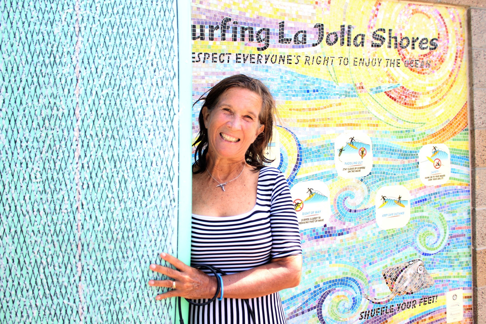 Lorraine Schmalenberger, president of the La Jolla Shores Surfing Association, poses with her board in front of a $10,000 mural that WindanSea Surf Club donated the fi